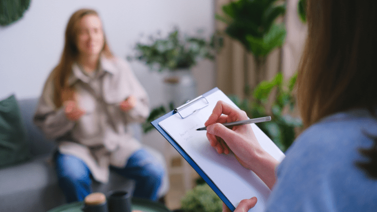 A person sitting on a couch with a pen in their hand and another person sitting next to them