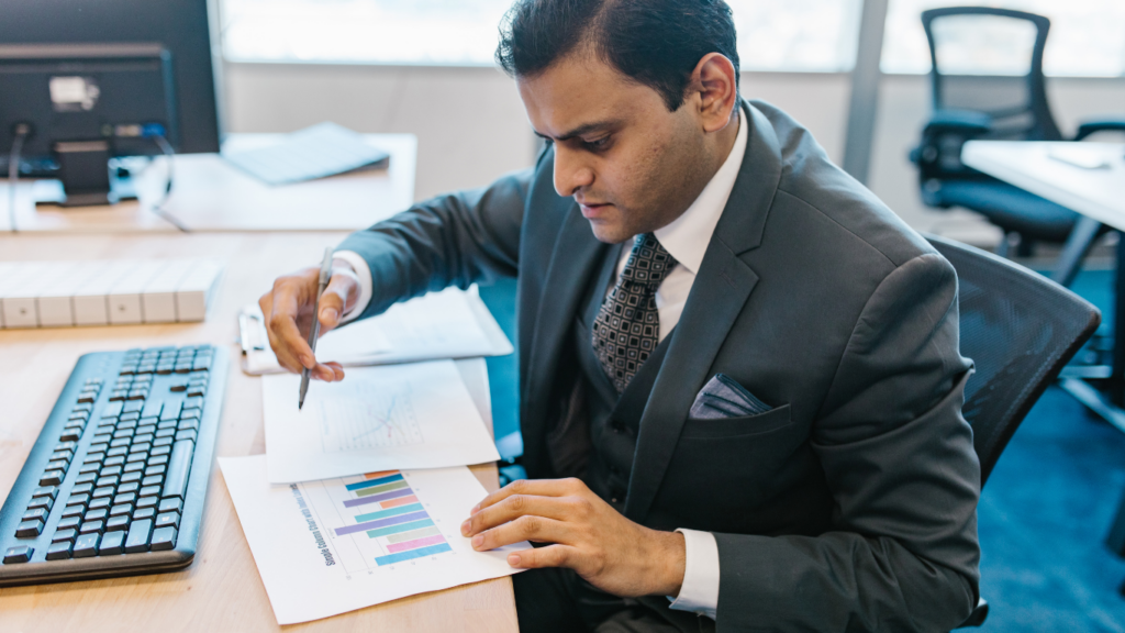 A person in a suit sitting at a desk with papers and a computer