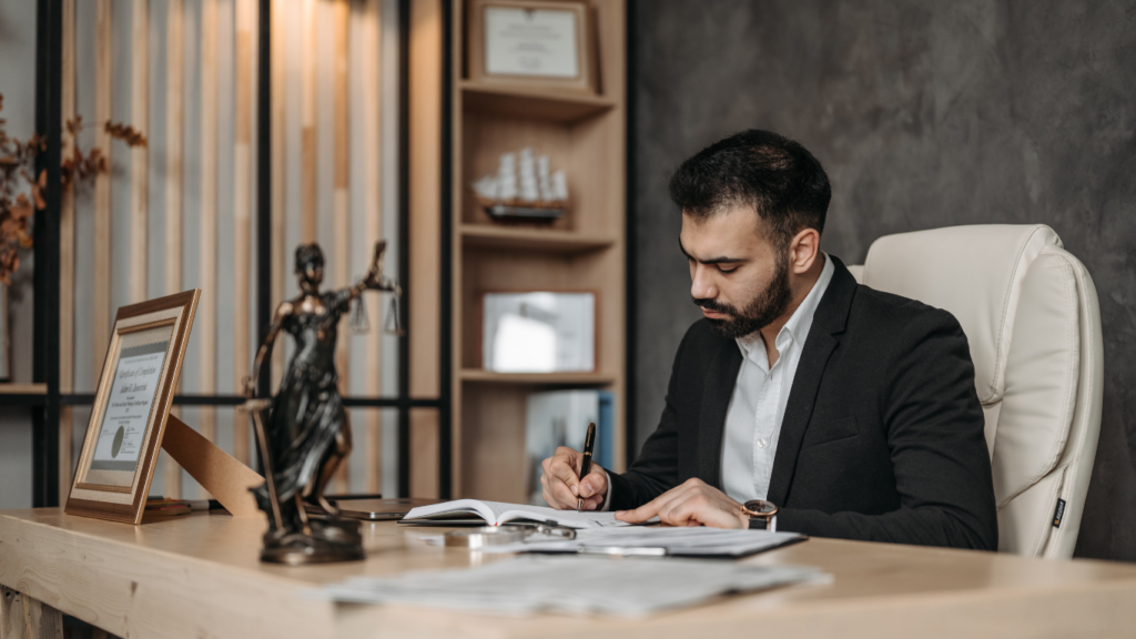 A person in a suit sitting at a desk writing on a piece of paper.